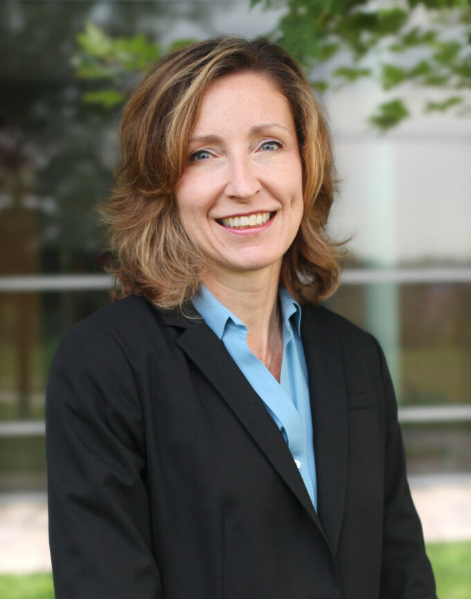Elizabeth Ransom smiles outside with shoulder-cropped brown hair, a dark suit jacket, and light blue button down shirt.
